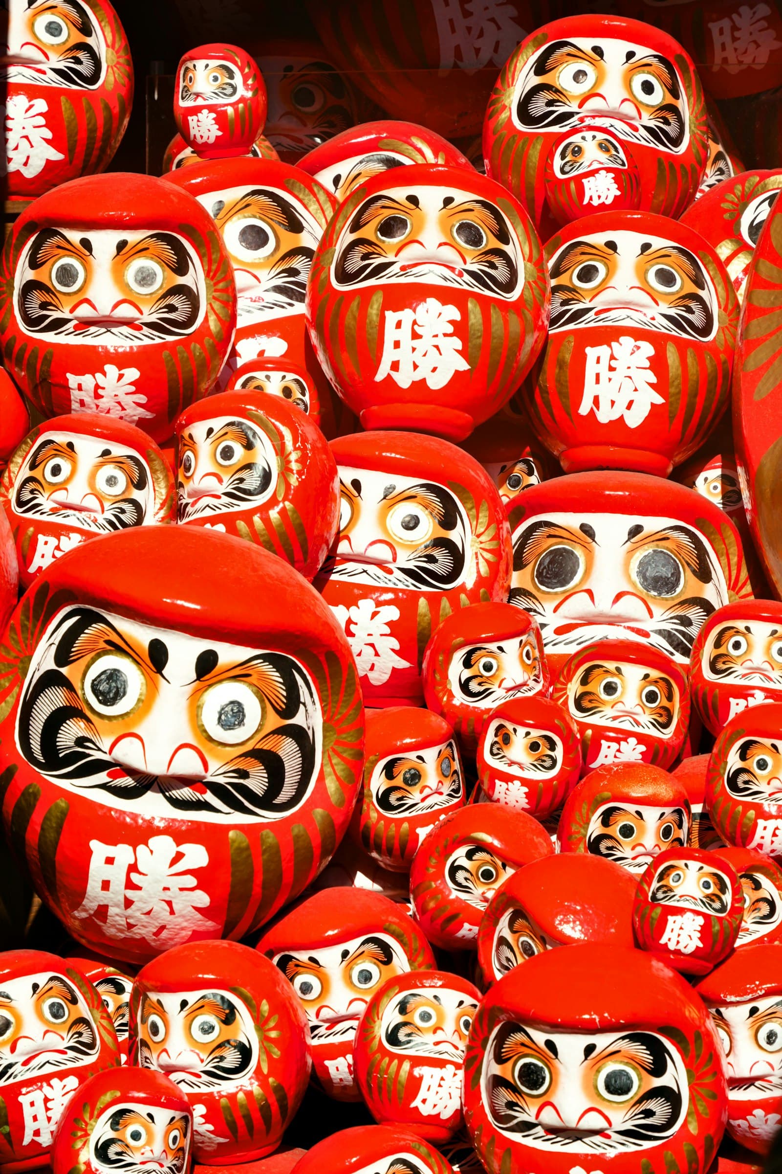 Muñecos daruma rojos con detalles dorados expuestos en Osaka, Japón.