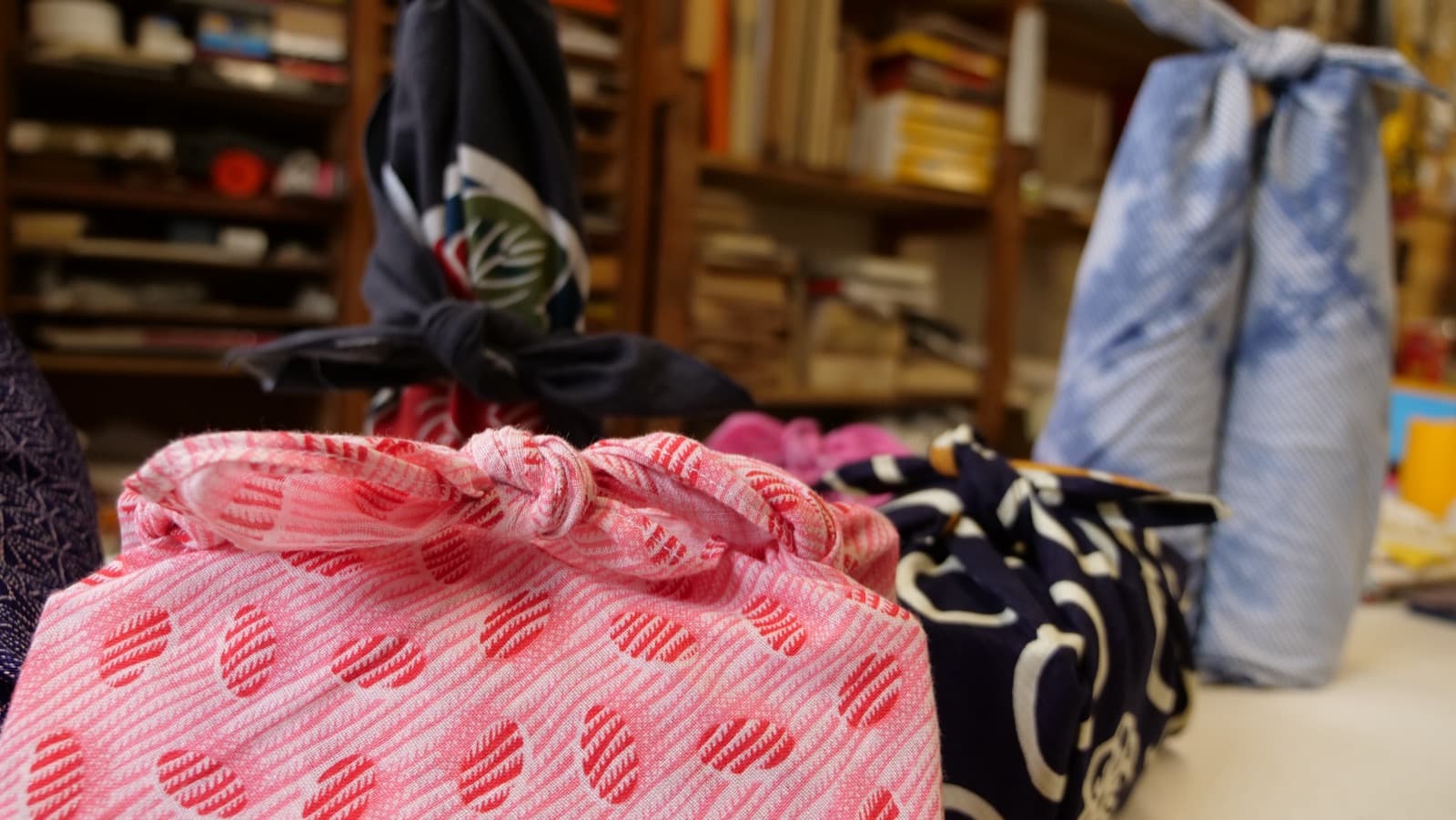 Hands demonstrating a traditional Japanese furoshiki cloth wrapping technique with patterned fabric.