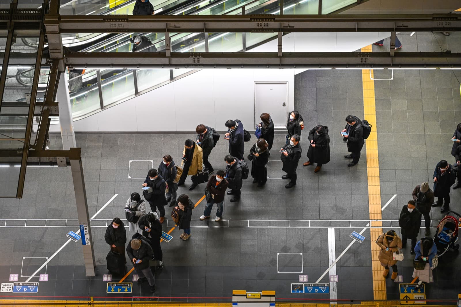 Passengers standing in an orderly queue on a train platform at Osaka Station in Japan.