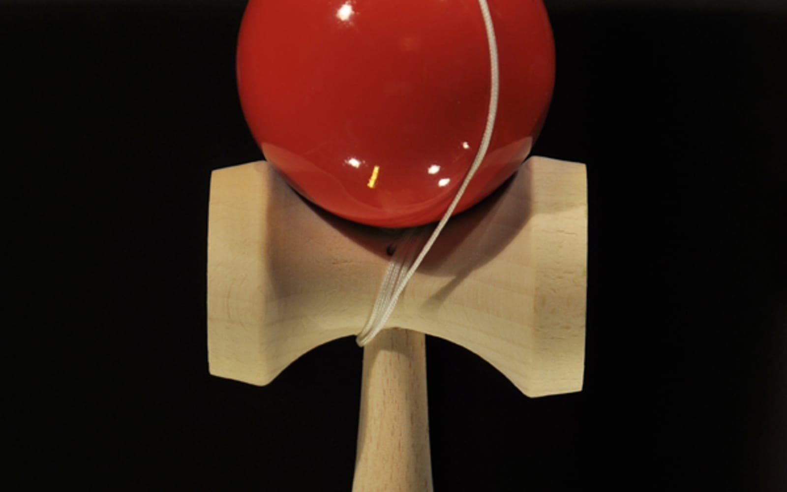 A red Japanese kendama skill toy with cup, spike, and ball.