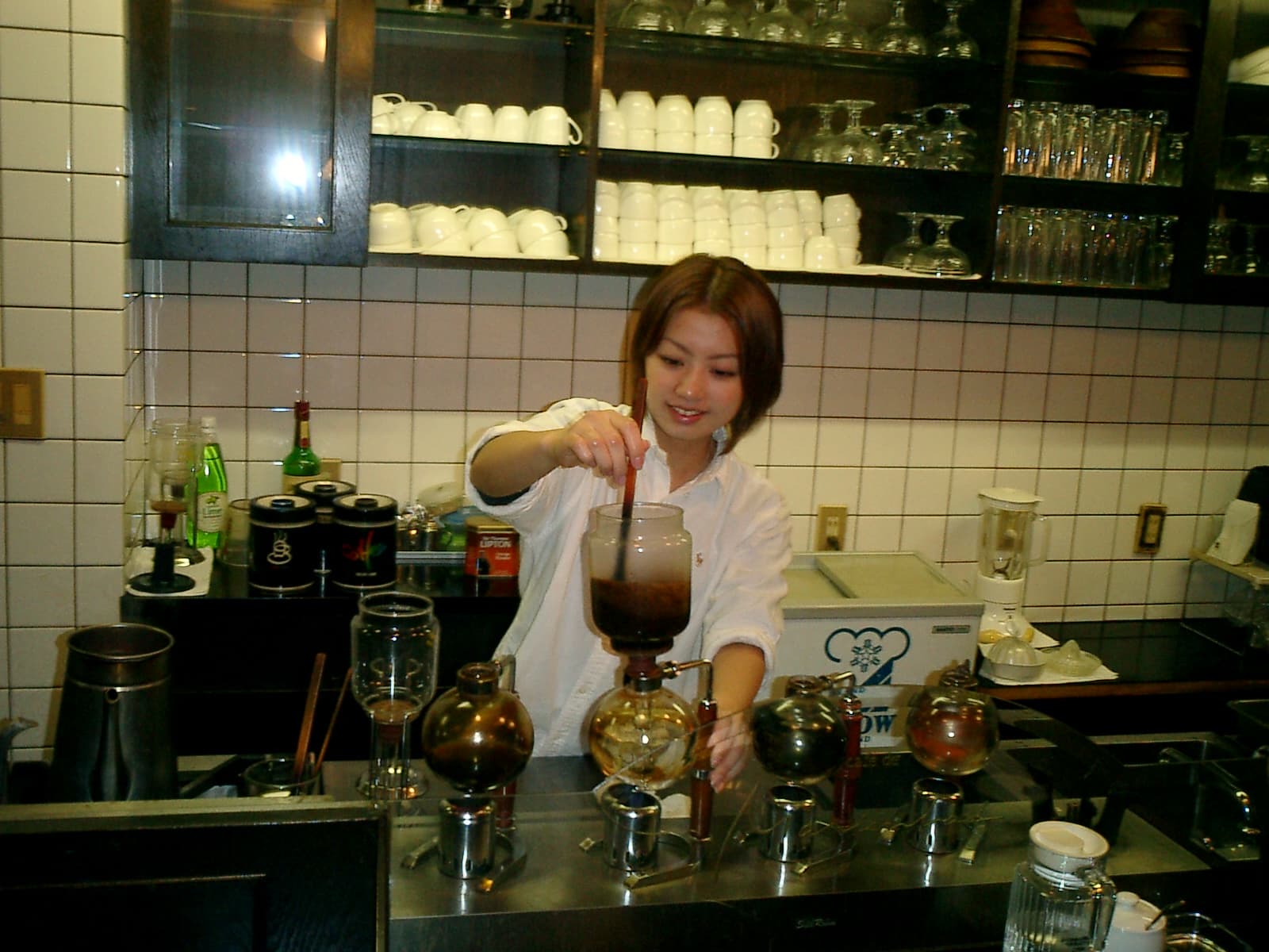 Interior de un café tradicional de Tokio con barra, utensilios de café y una barista trabajando.